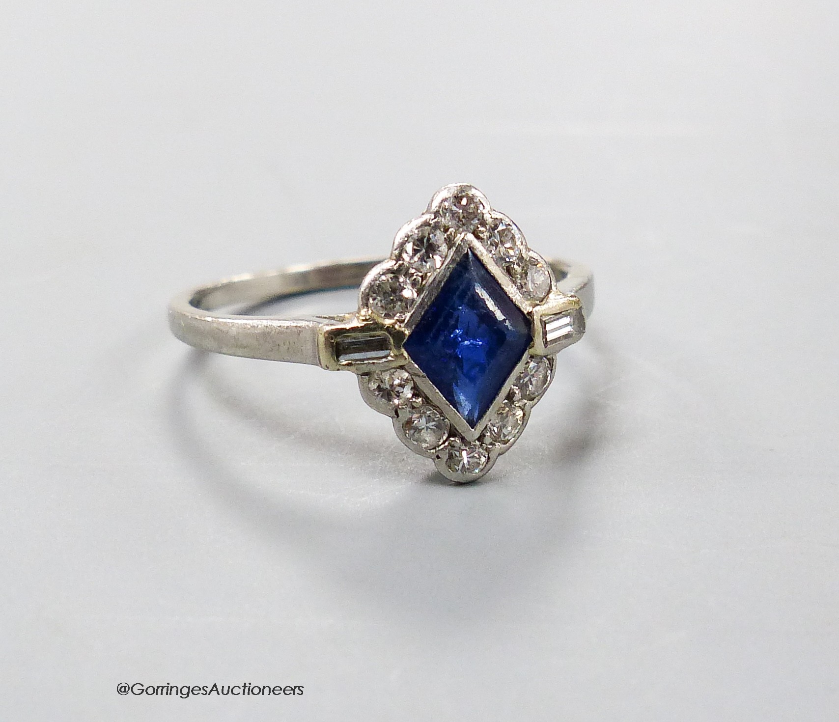 A 1920's white metal (stamped platinum), sapphire, baguette and round cut diamond cluster set lozenge shaped dress ring, size N/O, gross 3.3 grams.